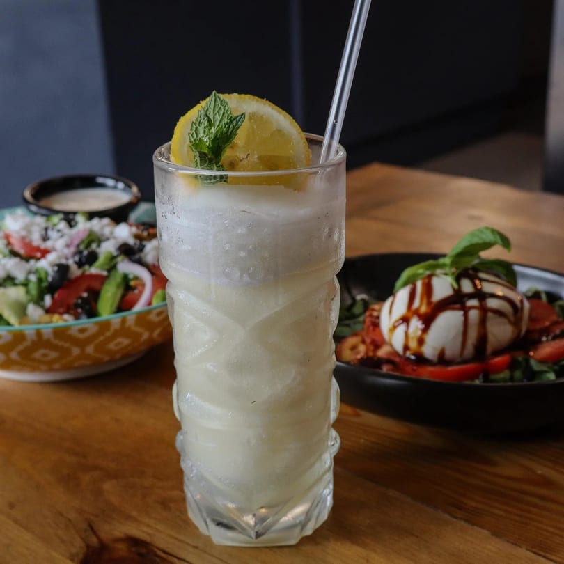A frosty drink with lemon and mint, a Greek salad, and burrata with balsamic glaze.