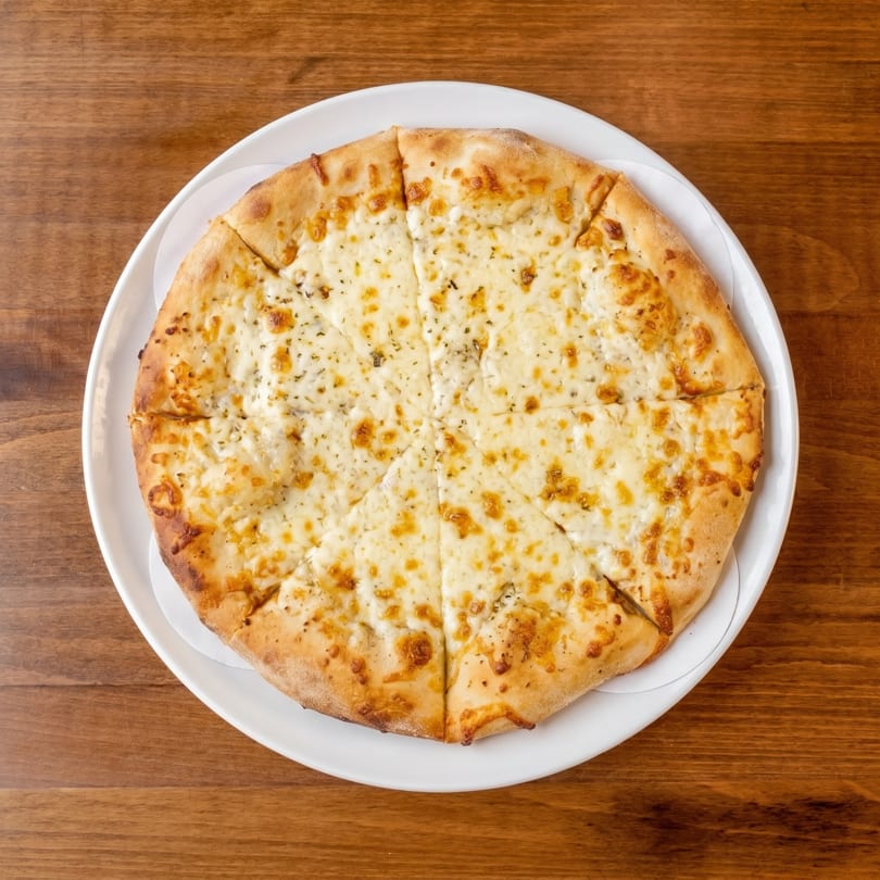 Overhead view of a sliced cheese pizza on a white plate, resting on a wooden table.