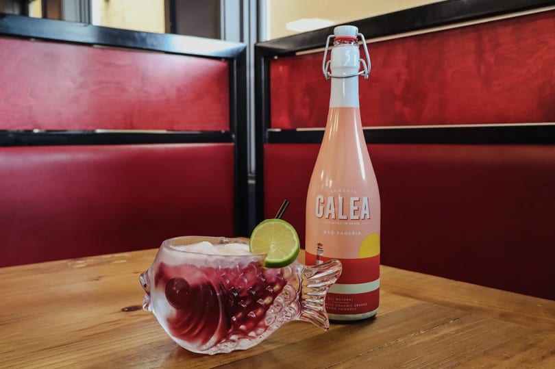 A fish-shaped glass of red sangria with lime and a bottle of Calea Red Sangria.