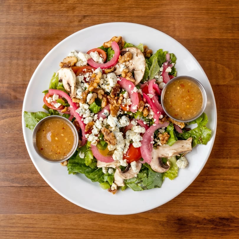 Overhead view of a vibrant salad with lettuce, mushrooms, tomatoes, pickled onions, walnuts, and feta cheese.